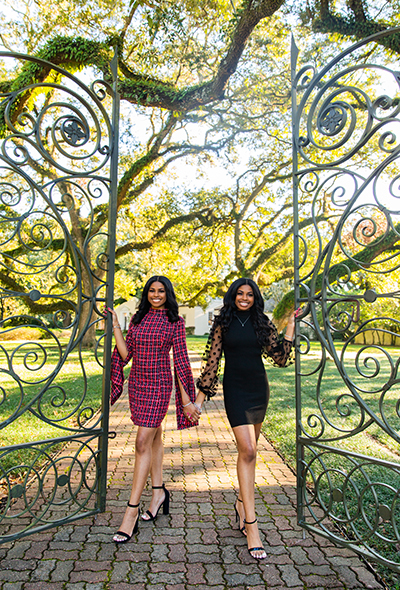 Two females take their graduation photos in front of the Alumni Center gates