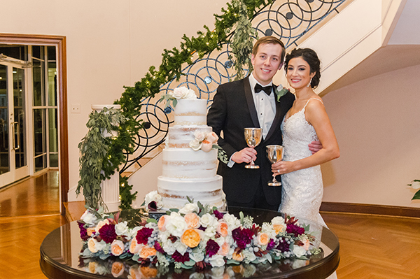 A bride and groom with their wedding cake, located in the Alumni Center foyer by the grand staircase